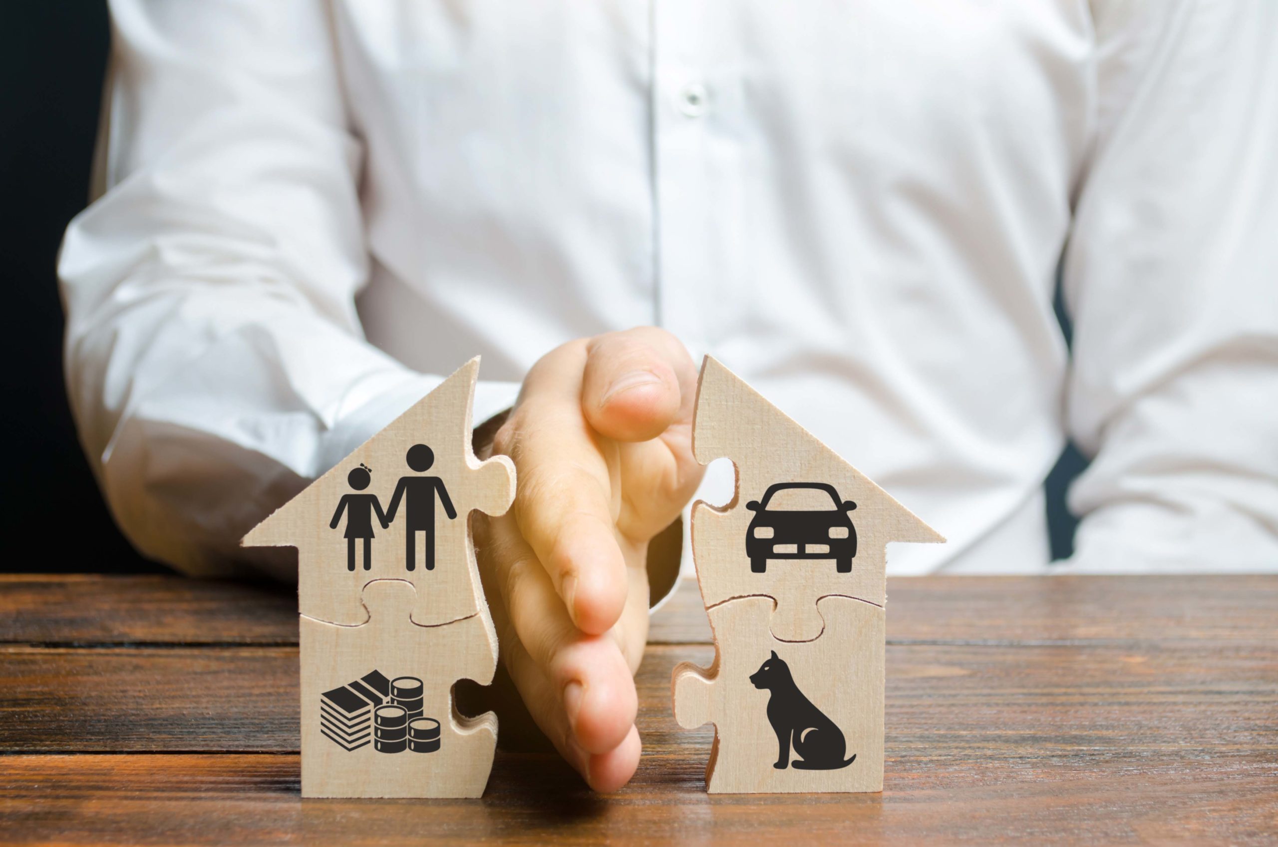 Ein Mann teilt ein Hausförmiges Puzzle mit seiner Hand in zwei Hälften. Symbol für das Scheidungsrecht, einen wichtigen Aspekt des Familienrechts.