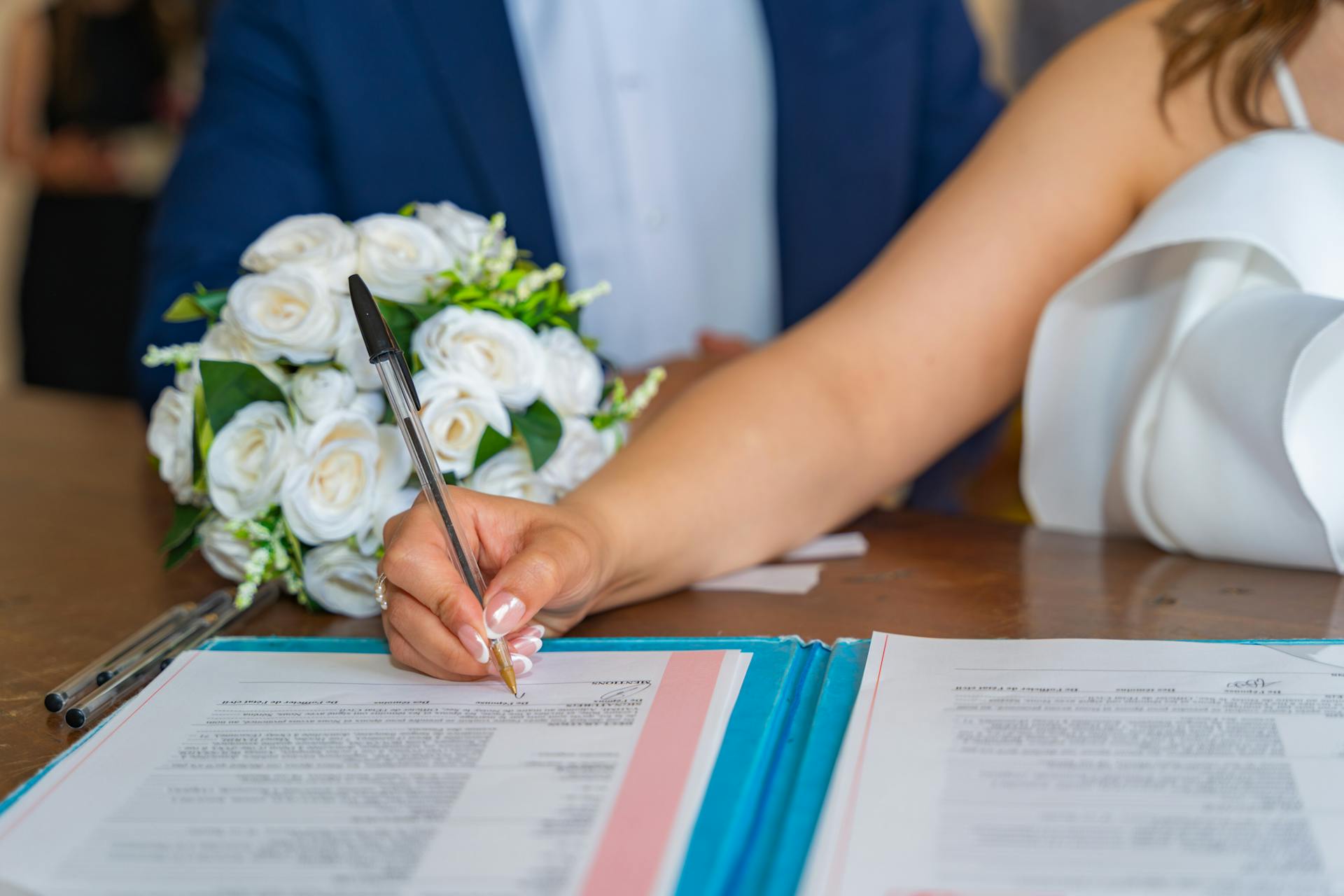 Ein Paar unterschreibt bei der Hochzeit ein Dokument. Die Kosten für den Ehevertrag sind bereits bezahlt.